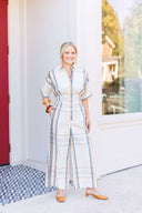 Woman in an ivory plaid jumpsuit with cinched waist.
