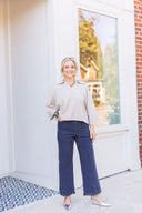 Woman wearing a beige collared pop-over sweater and black embroidered hem jeans.