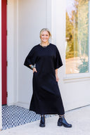 Woman wearing a black jersey maxi dress with half sleeves and pockets.