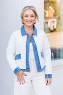 Woman wearing a white quilted jacket with blue denim accents in an indoor setting.