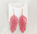 Pink feather-shaped earrings on a white card with 'Virtue' branding.