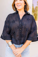 Woman wearing a black floral blouse with rolled-up sleeves, standing outdoors.