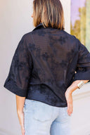 Woman wearing a black floral blouse and light blue jeans against a neutral background