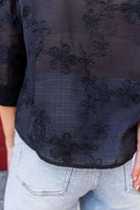 Black embroidered top worn by a person with light blue jeans.