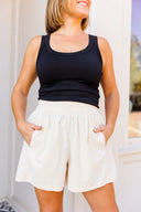 Woman wearing a black tank top and white corduroy shorts with a blurred background