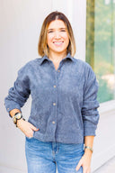 Woman wearing a gray corduroy shirt and jeans standing outdoors.