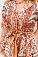 Woman wearing a floral dress with orange and red patterns on a plain background