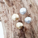 Four round earrings, two gold and two silver, on a wooden surface.