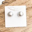 Pearl stud earrings on a branded card with a wooden background
