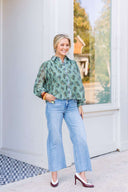 Woman wearing a long-sleeve green floral blouse and light blue jeans.