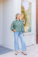 Woman wearing a long sleeve green floral blouse and blue jeans standing outside a building.
