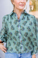Woman wearing a long sleeve green floral flowy blouse.