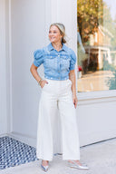 Woman wearing a short sleeve denim button-down shirt / jacket and ivory pants.