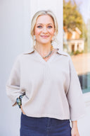 Woman wearing a beige collared sweater and black jeans.