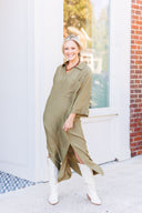 Woman wearing an olive green maxi shirt dress and white boots standing outdoors.