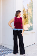 Maroon velvet top with blue feather trim paired with black denim.