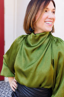 Woman wearing a green satin blouse with a blurred background