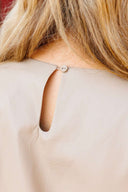 Close-up of a beige blouse with a button on a plain background