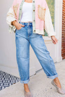 Person wearing a colorful fringe acket, white top, barrel blue jeans, and sparkly flats on a sidewalk.