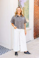 Woman wearing a leopard print shirt, white pants, and black sneakers standing in front of a building.
