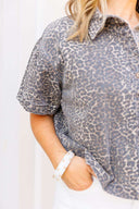 Woman wearing a leopard print shirt standing in front of white background.
