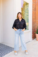 Woman wearing a black shirt and light blue jeans standing on a porch.