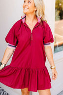 Woman wearing a crimson dress with a white wall and window in the background