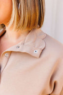 Close-up of a beige shirt with a scalloped collar and snaps on a neutral background
