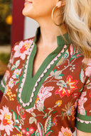 Close-up of a person wearing a floral dress with a brown background and green and light pink trim.