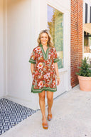 Woman in a floral dress walking outside a building with a plant in the background
