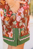Floral-patterned dress with green trim held by a hand.