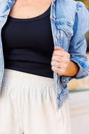 Person wearing a denim jacket, black top, and white corduroy shorts against a neutral background