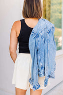 Person wearing a black tank top, white corduroy shorts, and a blue denim jacket outdoors.