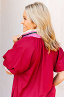 Woman wearing a crimson dress with a white wall and window in the background