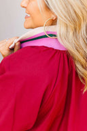 Close-up of a person wearing a crimson dress with a pink collar against a neutral background