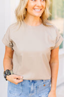 Woman wearing a beige top and blue jeans with a blurred outdoor background