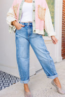 Person wearing a colorful fringe acket, white top, barrel blue jeans, and sparkly flats on a sidewalk.