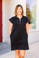 Woman wearing a black dress with studded details standing outside a building.