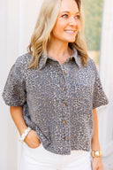 Woman wearing a leopard print shirt and white jeans standing in front of a building.