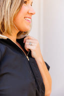 Woman wearing a black half zip top with a blurred background