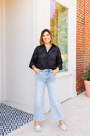 Woman wearing a black shirt and light blue jeans standing on a porch.