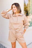 Woman wearing a beige outfit with a matching jacket and shorts, standing outdoors.