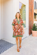 Woman in a floral dress walking outside a building with a plant in the background