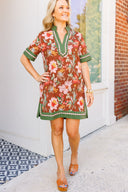 Woman wearing a floral dress with green trim standing on a sidewalk.