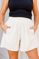 Person wearing a black top and white corduroy shorts against a neutral background