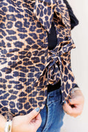 Woman wearing a leopard print vest with ruffled sleeve long sleeve underneath and blue jeans outdoors.