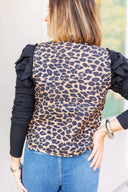 Woman wearing a leopard print vest with ruffled sleeve long sleeve underneath and blue jeans outdoors.