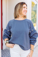 Woman wearing a gray sweatshirt with pearl embellishments, standing outside Laundry Dae Boutique.