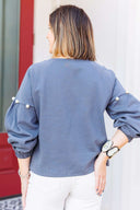 Woman wearing a gray sweatshirt with pearl embellishments, standing outside Laundry Dae Boutique.