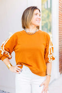 Woman wearing a toffee sweatshirt with white ribbon detail standing in front of Laundry Dae Boutique.